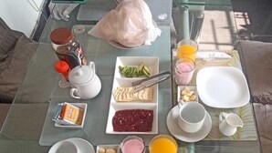 A breakfast setup on a glass table with various food items, utensils, and a teapot. - Casita Libertad Barranco (Lima)