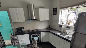 A kitchen with white cabinets, a stainless steel range hood, a microwave, and a refrigerator. - Casita Libertad Barranco (Lima)