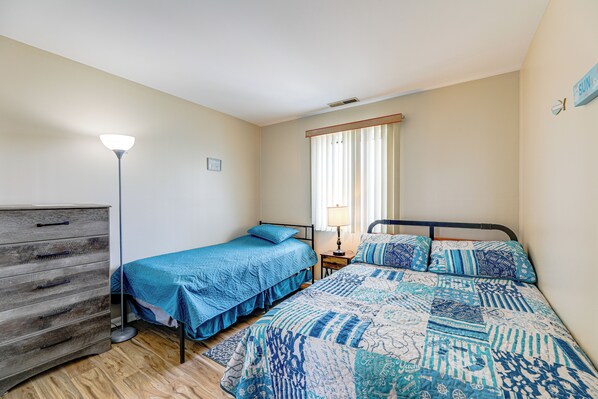 Une chambre avec deux lits, une commode, une lampe et une fenêtre avec des rideaux.
