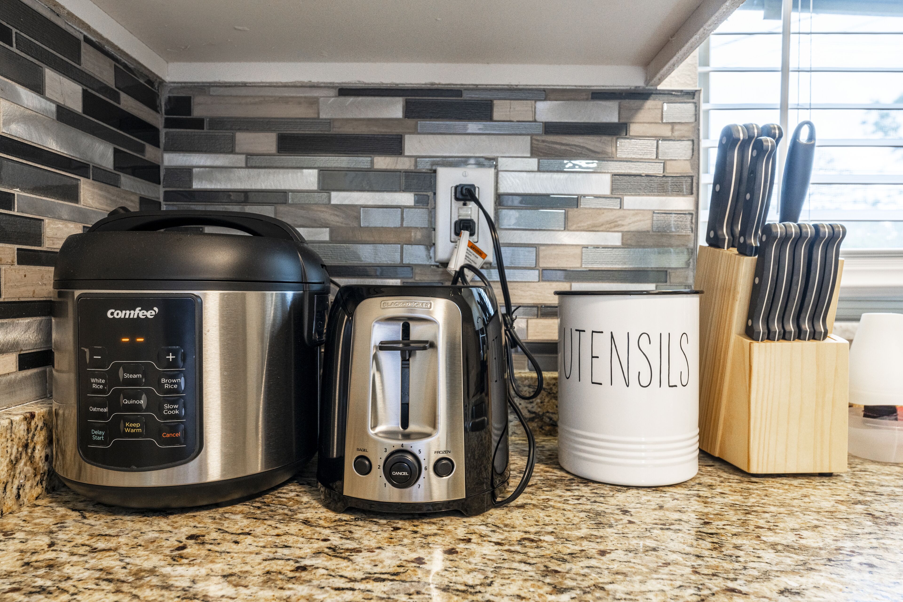 Eine Küchenarbeitsplatte mit einem Comfee-Reiskocher, einem Toaster und einer weißen Tasse mit dem Aufdruck 'UTENSILS'.