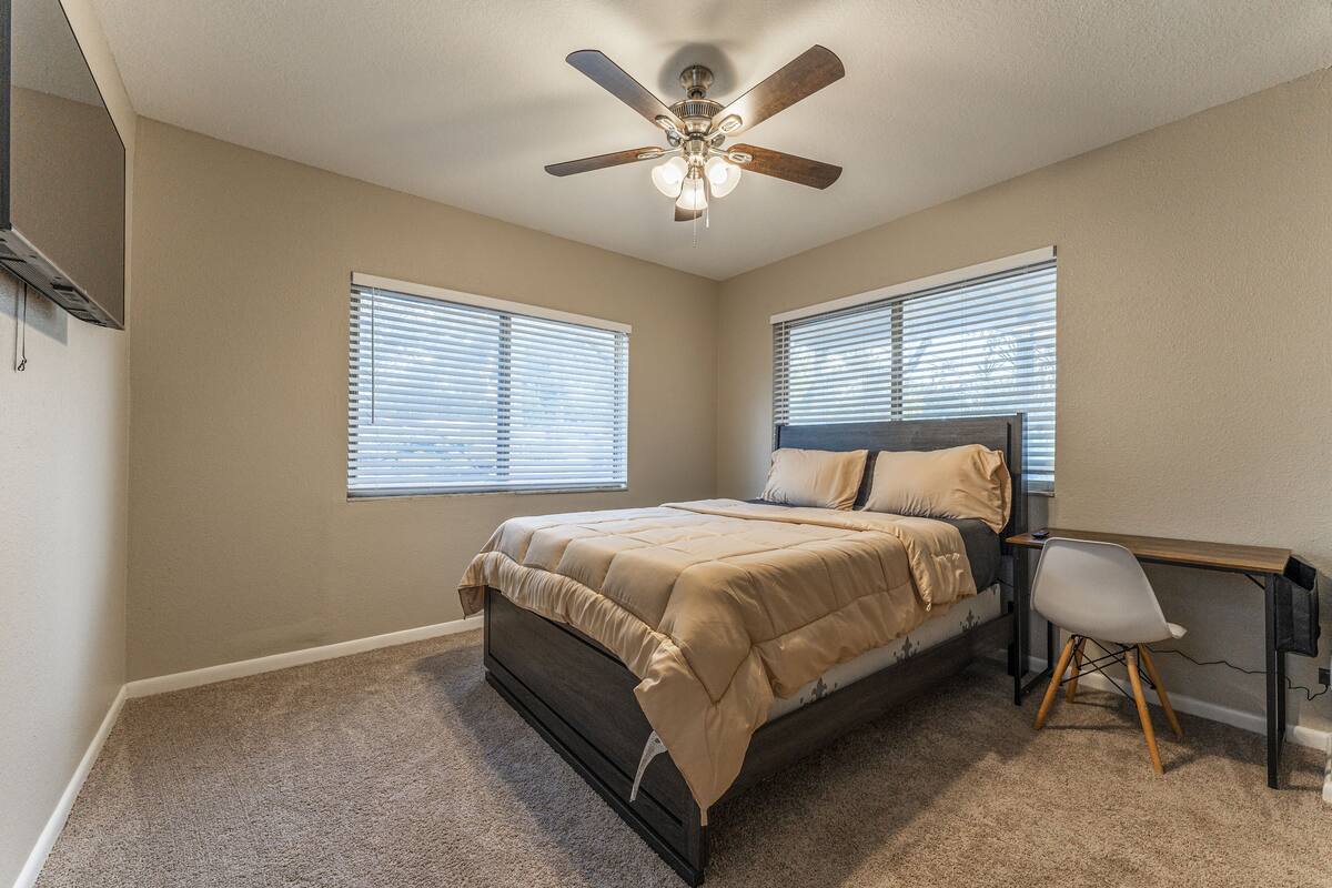 A bedroom with a bed, a desk, a chair, and a ceiling fan.