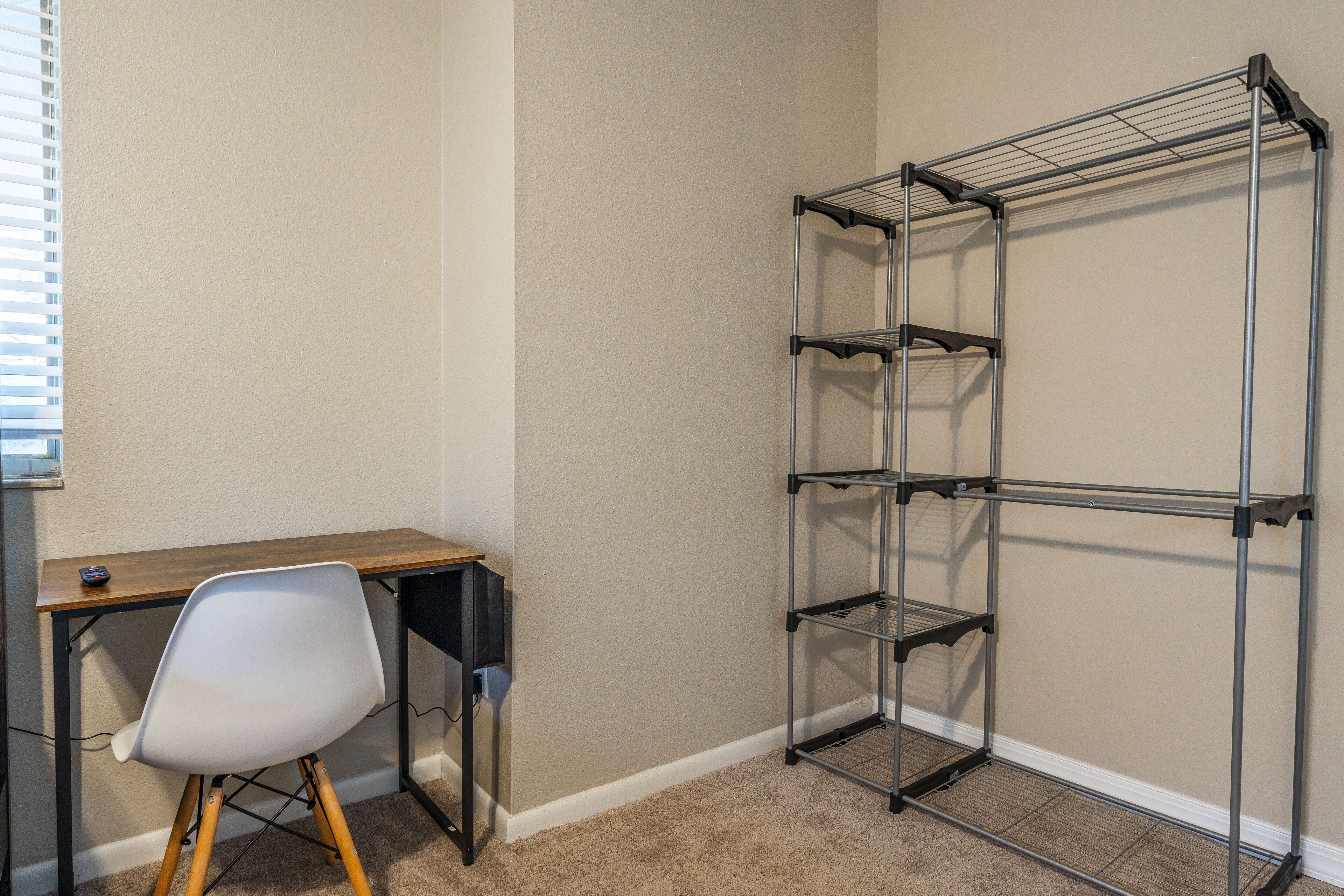 Habitación de esquina con escritorio, silla y estantería metálica adosada a la pared.