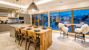 A modern kitchen with a large island, wooden chairs, and a view of a snowy mountain through large windows. - Gente del Sur - Fique (Ushuaia)