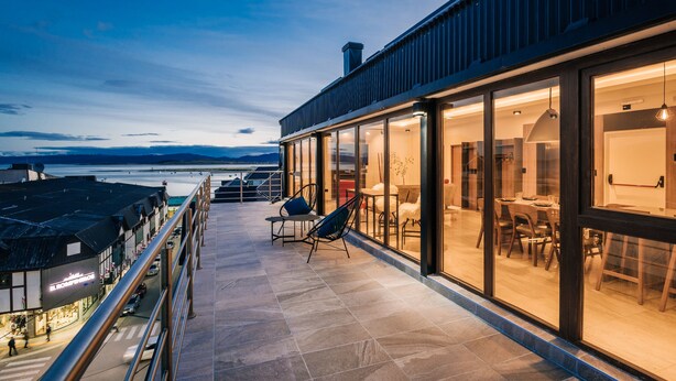 A modern building with a glass exterior, a terrace with seating, and a view of the water. - Gente del Sur - Fique (Ushuaia)