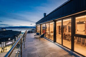 A modern building with a glass exterior, a terrace with seating, and a view of the water. - Gente del Sur - Fique (Ushuaia)