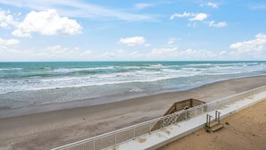 Une plage avec une rambarde, des vagues et un ciel dégagé.