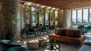 A modern lounge area with teal chairs, a brown sofa, and a large window with a view of palm trees and buildings. - WealthyStays: SkyHigh Central (Nicosia)