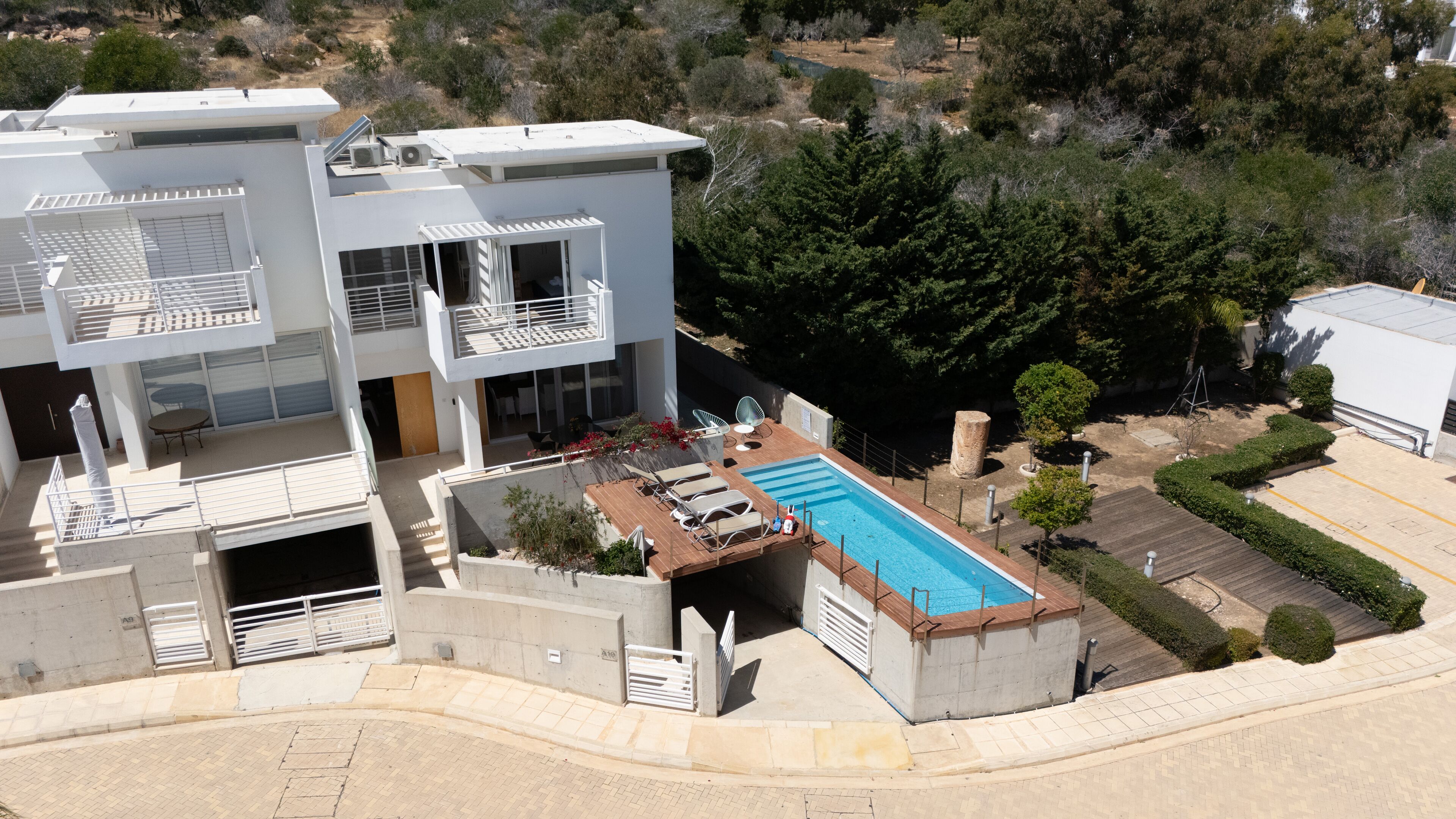 A modern two-story building with a rooftop pool, outdoor seating, and a view of the surrounding landscape.