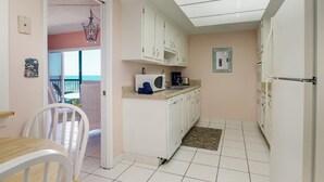 A compact kitchen with white cabinets, a microwave, and a coffee maker. There is a small dining area with a white chair and a table. - You cannot get any closer to the beach! 2BR condo (Satellite Beach)