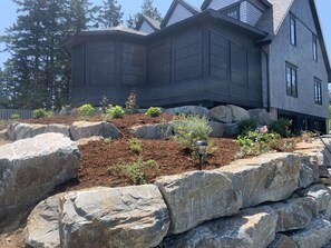 Una casa moderna con jardín ajardinado, rocas grandes y diversas plantas.