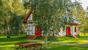 Ein traditionelles Holzhaus mit roter Tür, umgeben von üppiger Vegetation und einer Bank im Vordergrund.