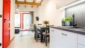Eine moderne Küche mit weißen Schränken, einer grauen Arbeitsplatte und einem Edelstahl-Spülbecken. Es gibt einen Essbereich mit Tisch und Stühlen, und eine rote Tür, die in einen anderen Raum führt.