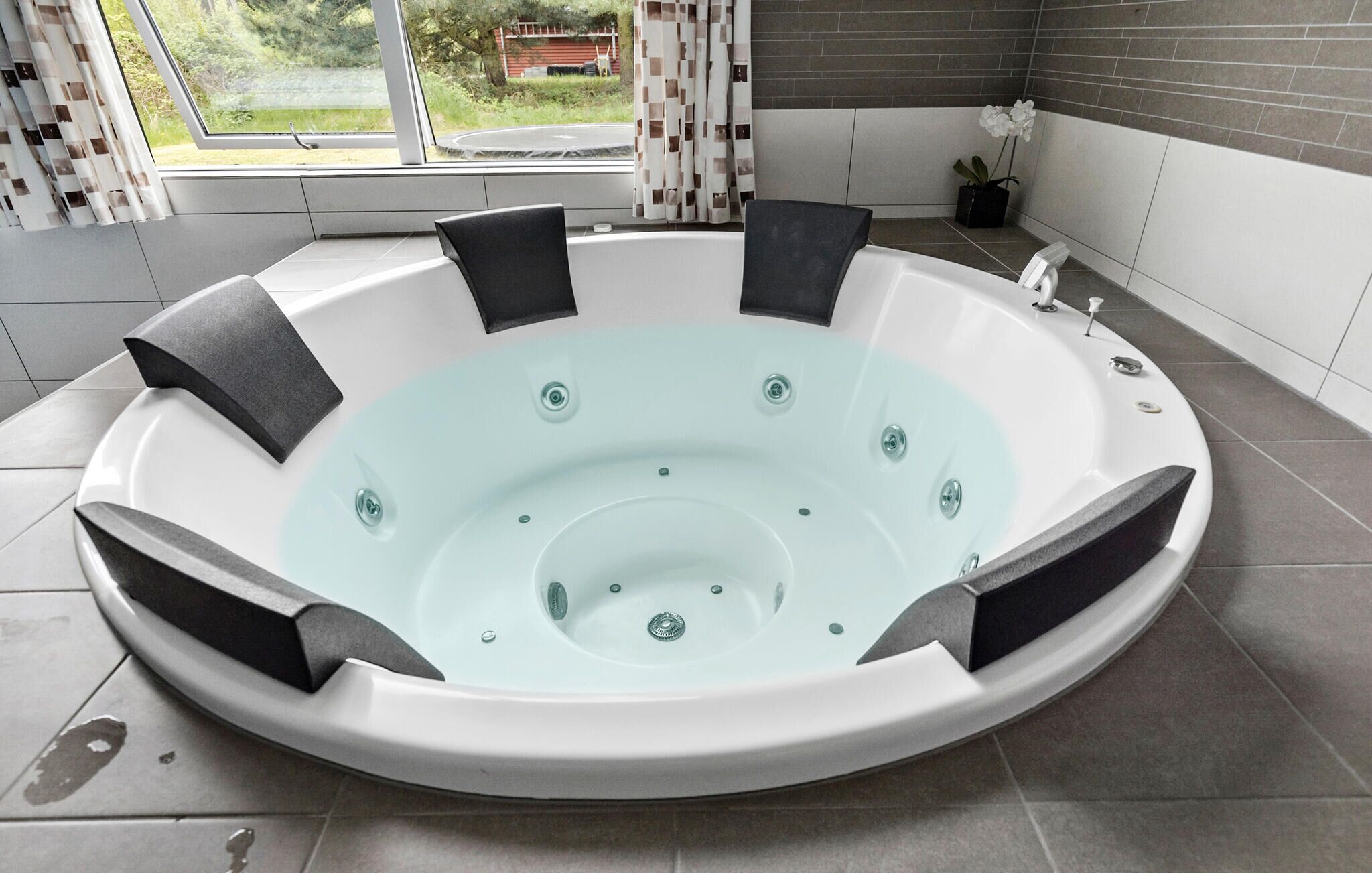 Une salle de bain moderne avec une baignoire sur pieds, une orchidée en pot et une vue sur un paysage verdoyant par la fenêtre.