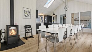 A modern dining area with a long table, white chairs, a black stove, and a skylight.