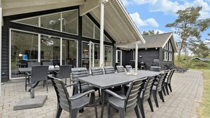 An outdoor dining area with a large table and chairs, a grill, and a covered patio.