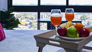 Bandeja de desayuno con frutas y dos vasos de jugo de naranja sobre una mesa junto a una ventana con vistas a la ciudad.
