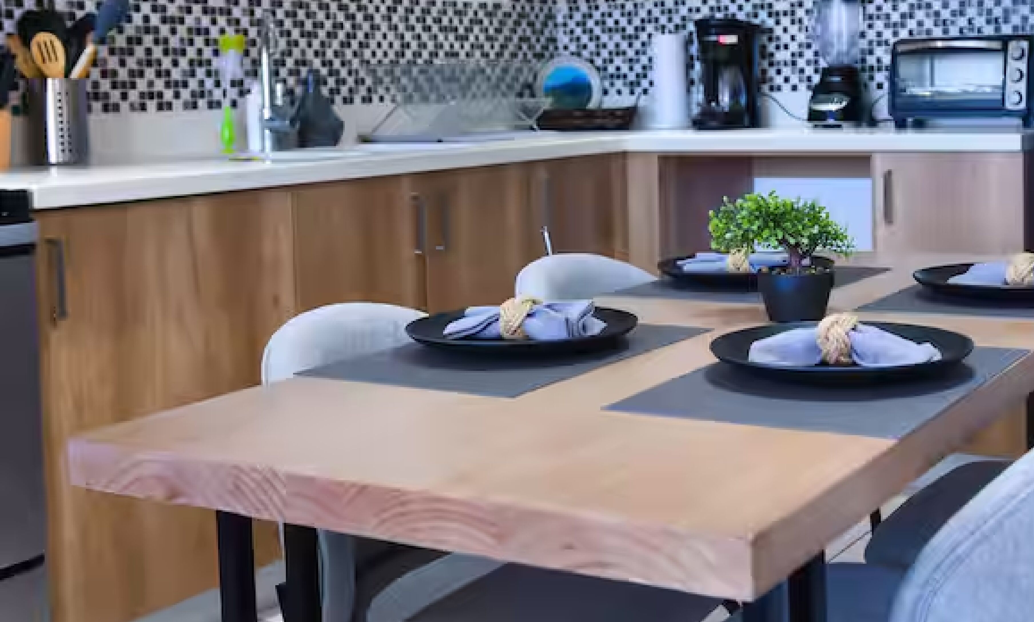 Une cuisine moderne avec des meubles en bois, un plan de travail blanc et un coin repas agrémenté d’assiettes et de serviettes.