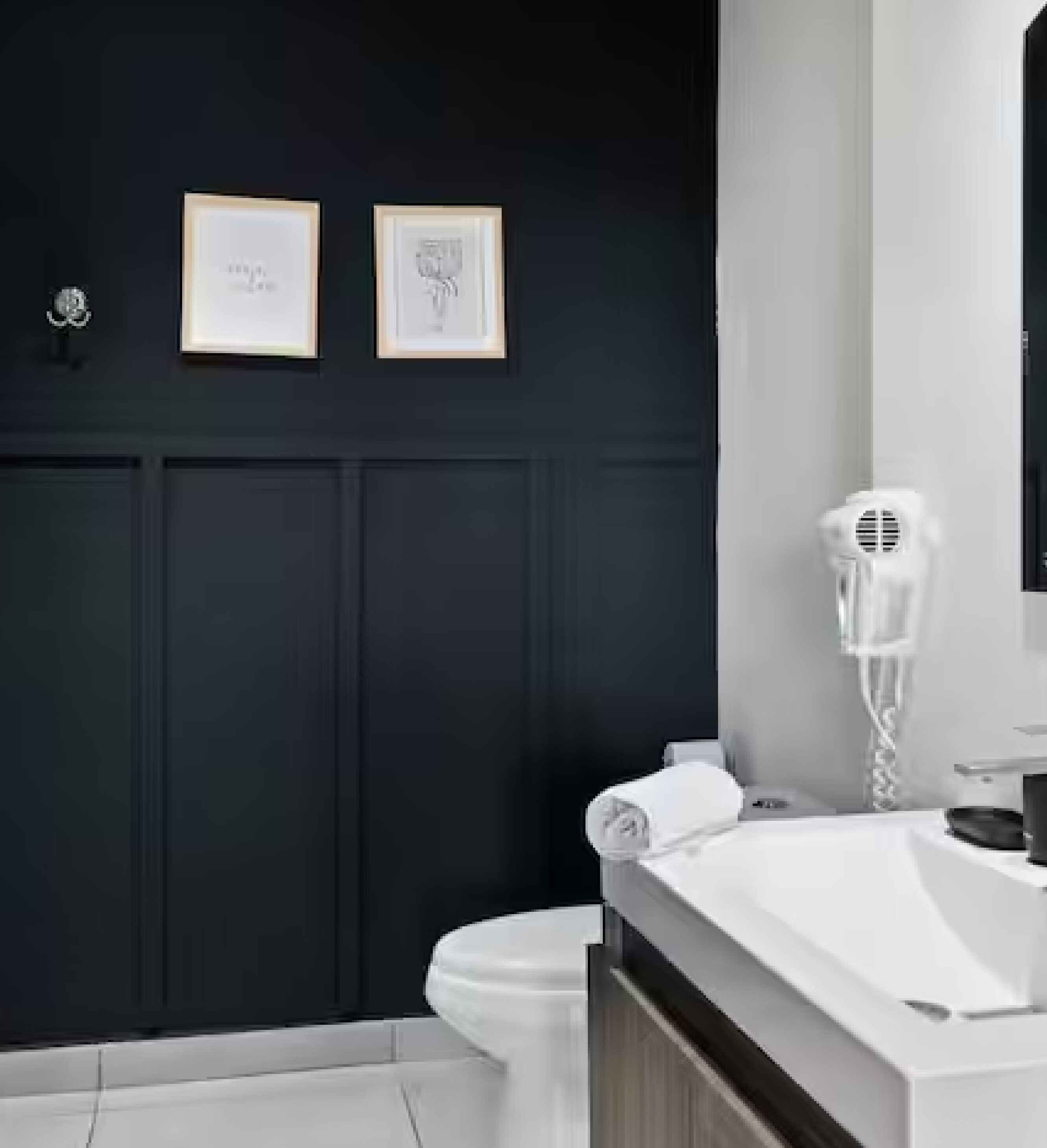 Une salle de bain moderne avec des murs sombres, un lavabo blanc et un sèche-cheveux posé sur le comptoir.