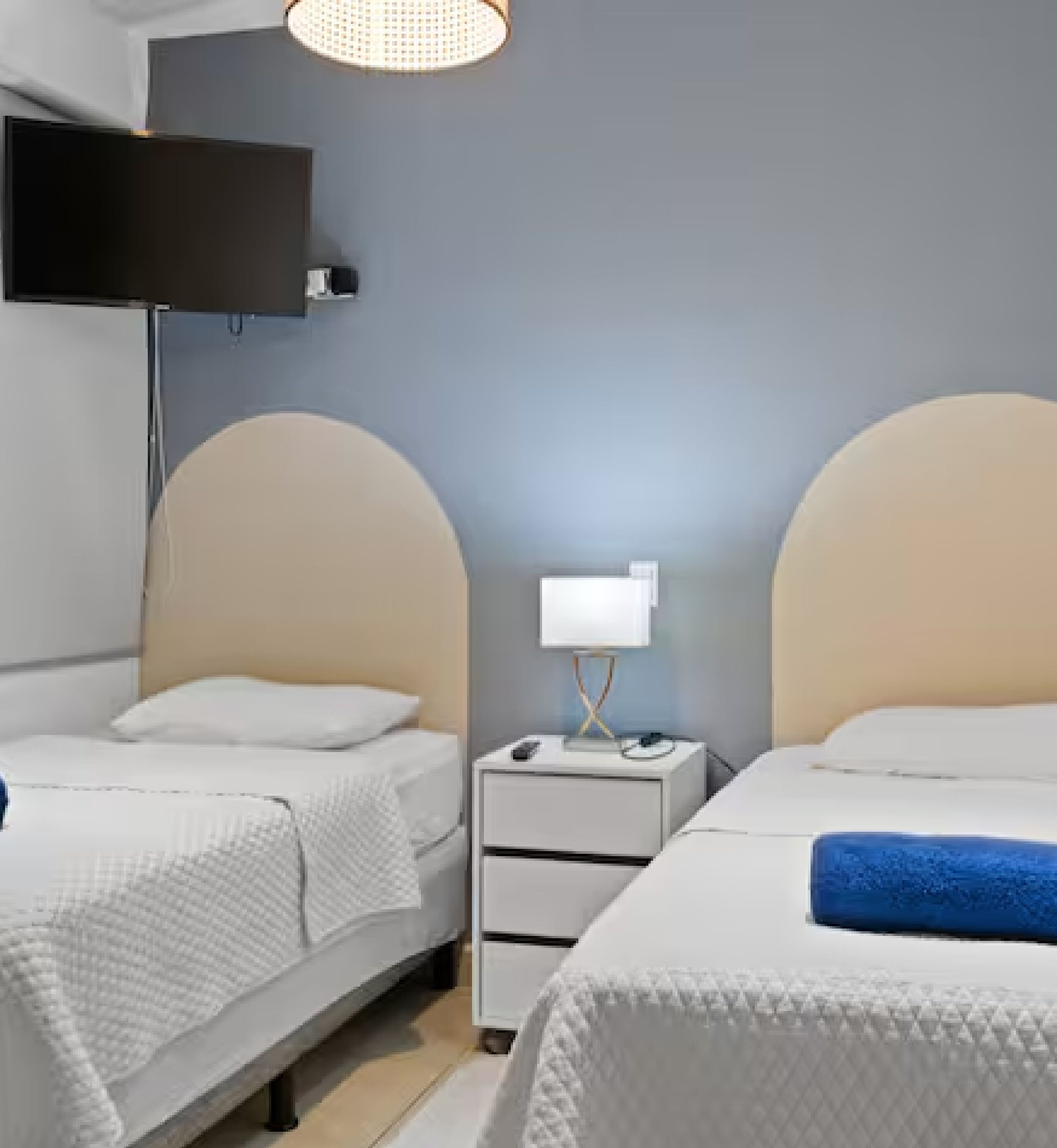 Ein Hotelzimmer mit zwei Betten, einem an der Wand montierten Fernseher und einem Nachttisch mit Lampe.