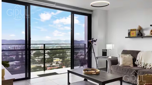 Un salón amplio con un gran ventanal corredero que da a un balcón con vistas a la ciudad.