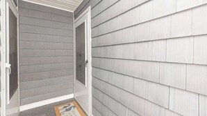 A covered entryway with a gray siding exterior, a door, and a doormat with text.