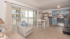 A living room with a sofa, a dining table with chairs, a kitchen with cabinets and appliances, and a balcony with railings.