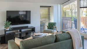 A modern living room with a flat-screen TV on a dark console, a green sofa, a small coffee table, and a chair with a green cushion.