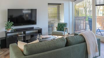Een moderne woonkamer met een flatscreen televisie op een donkere console, een groene bank, een klein bijzettafeltje en een stoel met een groen kussen.