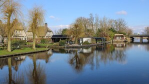A canal with a bridge, a thatched-roof building, and a modern structure with a sign.