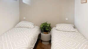 A small, simple room with two beds, a small table with a plant, and a window.