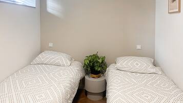 Een kleine, eenvoudige kamer met twee bedden, een tafeltje met een plant en een raam.