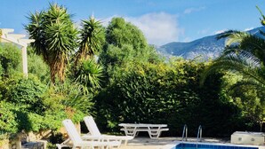 Une piscine dont les bords sont recouverts de carreaux, entourée de verdure et bordée d’un mur en pierre.