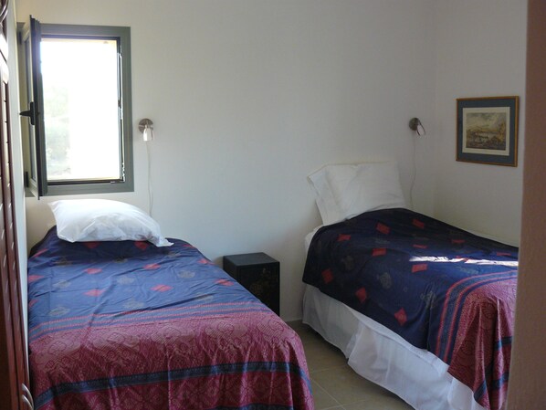 A room with two beds, one with a patterned bedspread and the other with a plain white pillow. There is a small bedside table between the beds, and a window on the left side. - Relax in Luxury and Beauty. Private Pool Panoramic views. Spacious modern villa (Kefalonia)