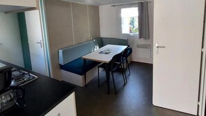 A compact kitchen with a gas stove, a dining area with a table and chairs, and a built-in bench. - Mobil Home - N025 (Bootzheim)