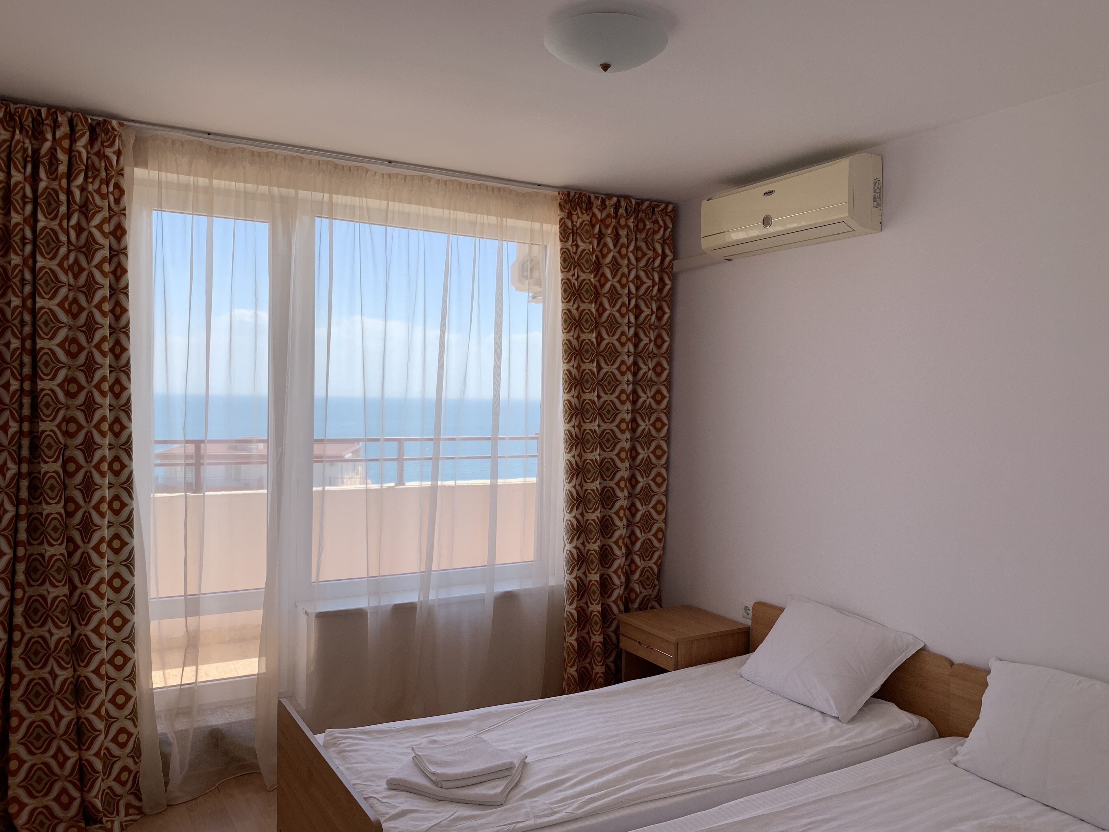 Una camera d'albergo con un letto, un comodino, una finestra con tende e un condizionatore d'aria a parete.