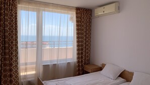 Habitación de hotel con cama, mesita de noche, ventana con cortinas y aire acondicionado en la pared.