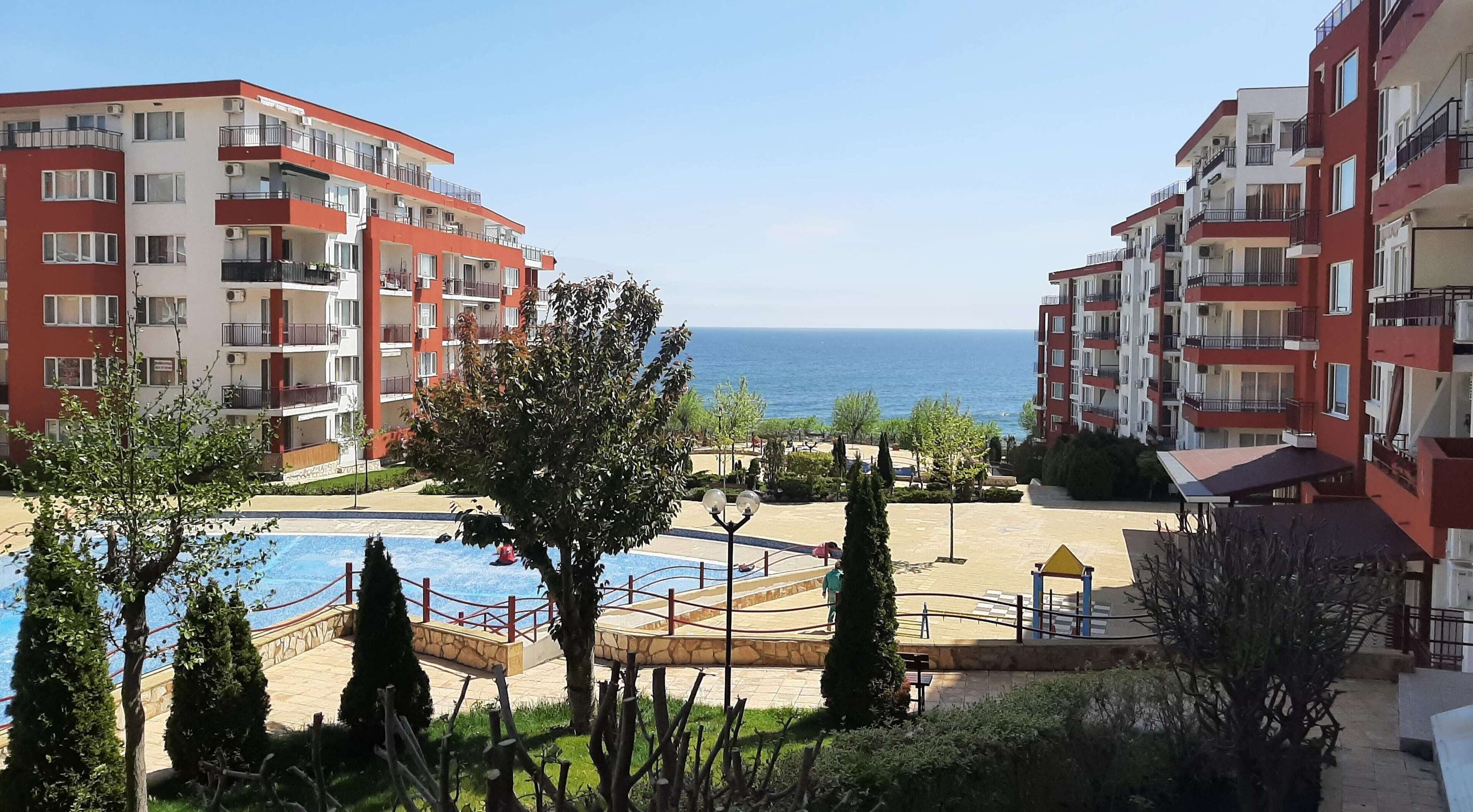 A residential building with balconies, a swimming pool, and a view of the sea.