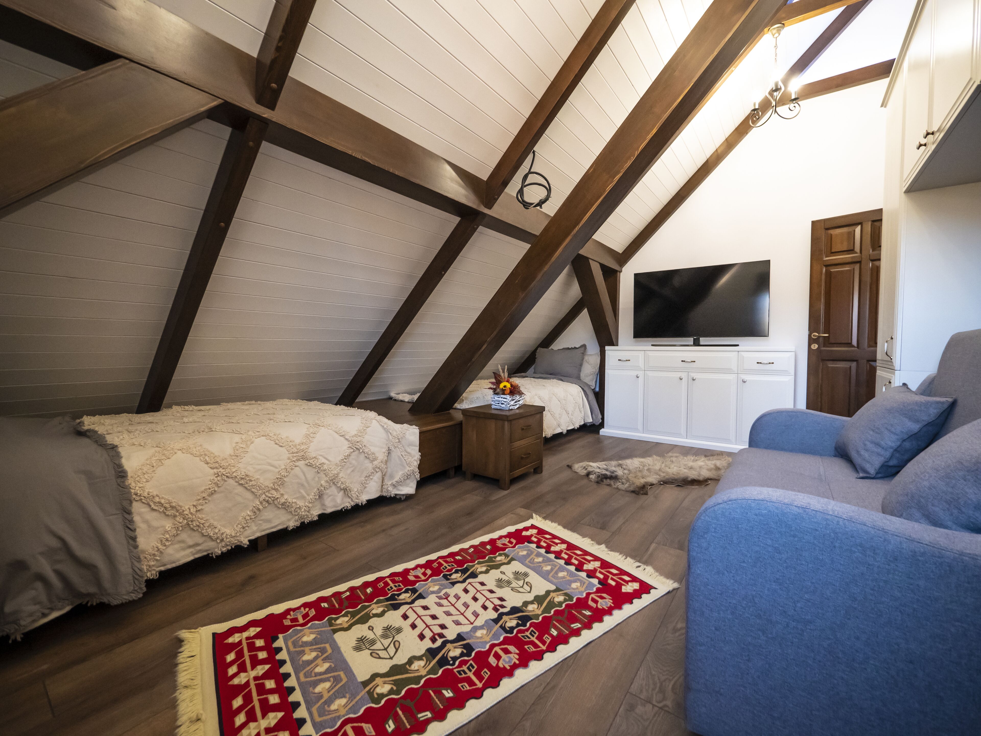 Een slaapkamer met zolderkamergevoel, een schuine kap, een televisie, een bank en een kamerkleed met een patroon.
