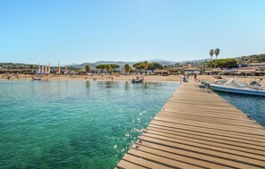 Un muelle de madera se extiende sobre aguas turquesas cristalinas, con barcos amarrados a la derecha.