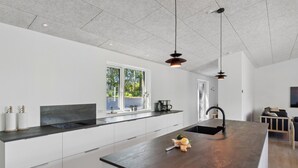 A modern kitchen with a large island, pendant lights, and a window providing a view of greenery.