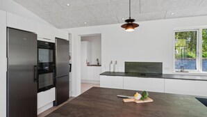 A modern kitchen with a large island, stainless steel appliances, and a view of greenery outside.