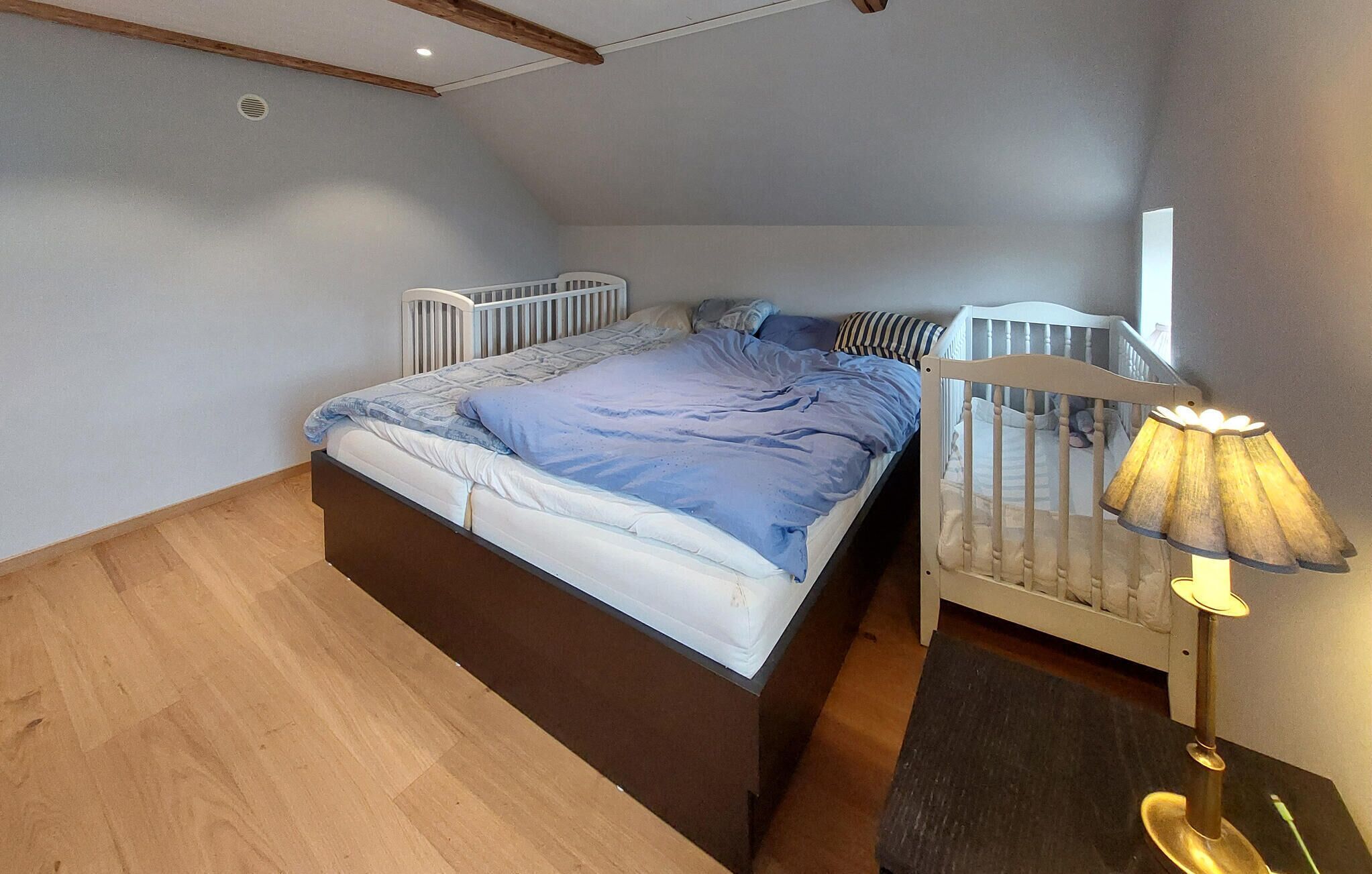 A bedroom with a bed, a nightstand, a lamp, and a crib.