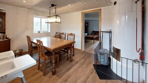 Un comedor con una mesa y sillas de madera, una lámpara colgante y vista a una sala de estar a través de un vano abierto.
