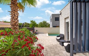 Un patio moderno al aire libre con piscina, mobiliario de mimbre y una palmera.