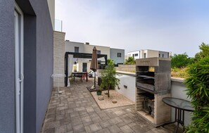 Un patio exterior moderno con área de barbacoa, asientos y un pequeño jardín.