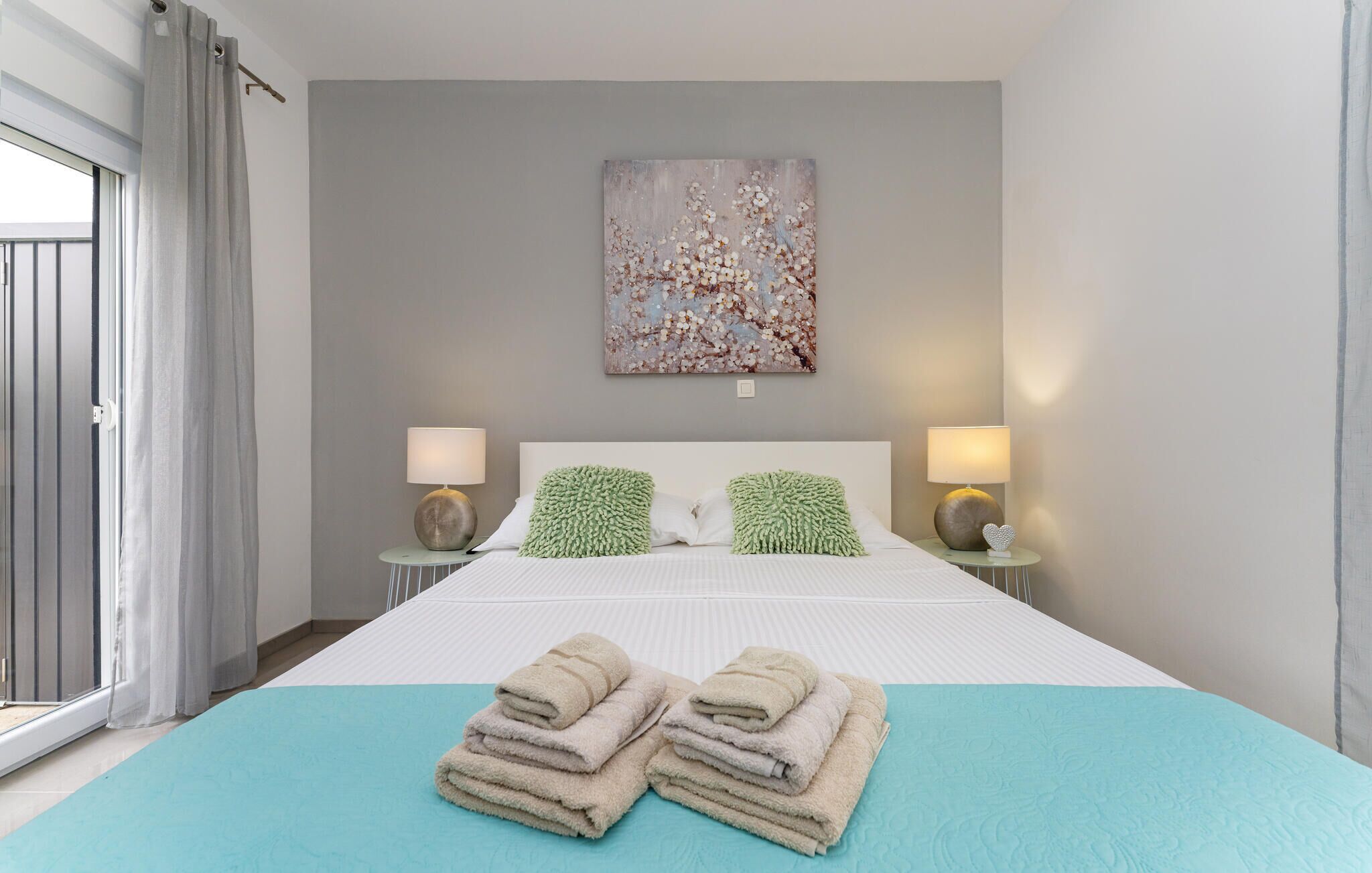A hotel room with a bed, two bedside tables with lamps, a painting on the wall, and a window with curtains.