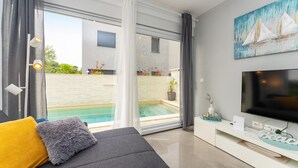 A modern living room with a grey sofa, a flat-screen TV, and a pool view. - Stunning home in Zaton (Zaton)