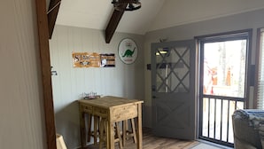 A room with a wooden table and chairs, a door with a glass panel, and wall decorations including a dinosaur and a gas station sign. - Pine Ridge retreat on Beech Mountain, quiet with fireplace and mountain views! (Beech Mountain)