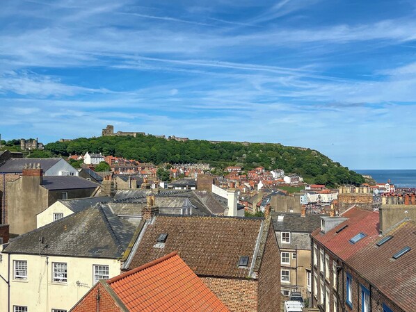 Un pueblo costero con edificios históricos, una fortaleza en la cima de una colina y vistas al mar.