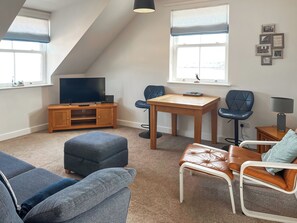 Habitación estilo loft con televisor, mueble de entretenimiento de madera, dos sofás, una mesa de comedor y un ventanal con persianas.